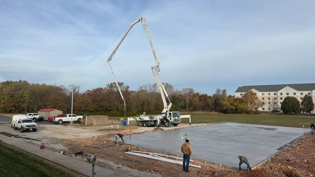 Construction site with concrete pouring by a pump truck, workers preparing a foundation slab.