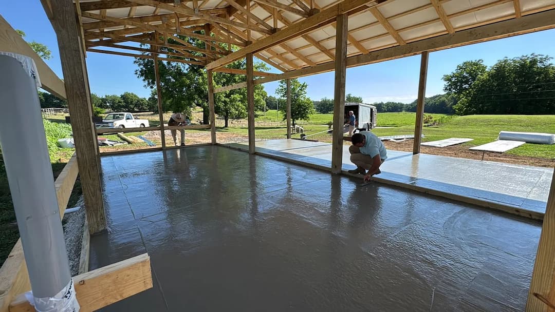 Workers pouring concrete in a partially constructed building surrounded by greenery.