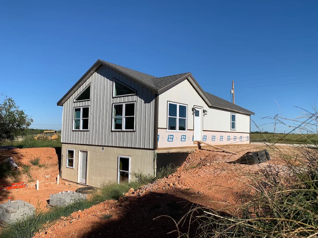 Modern two-story home under construction, featuring large windows and a gravel foundation.