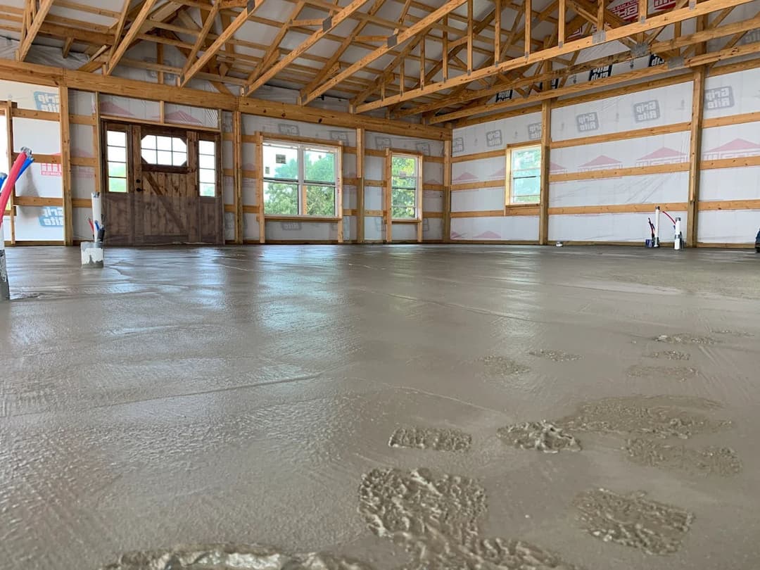Freshly poured concrete floor in a spacious wooden-framed building under construction.
