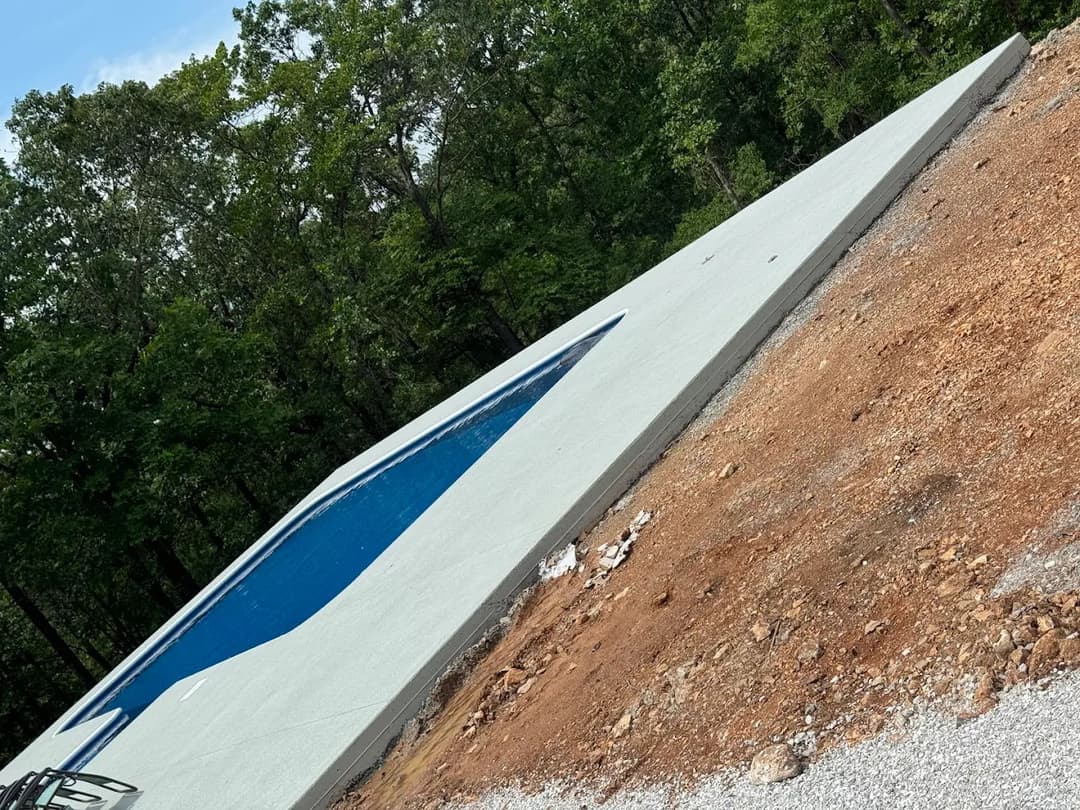 Newly constructed swimming pool surrounded by trees and unfinished landscape.