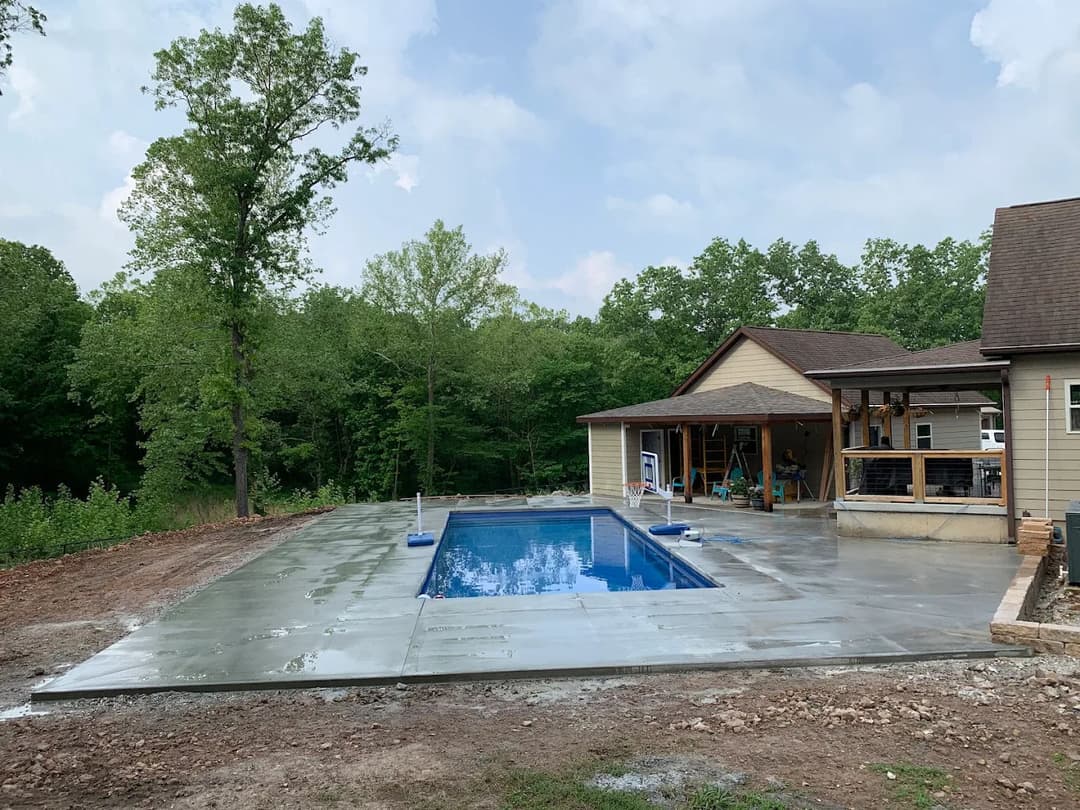 Newly installed in-ground pool surrounded by concrete patio and natural forest backdrop.